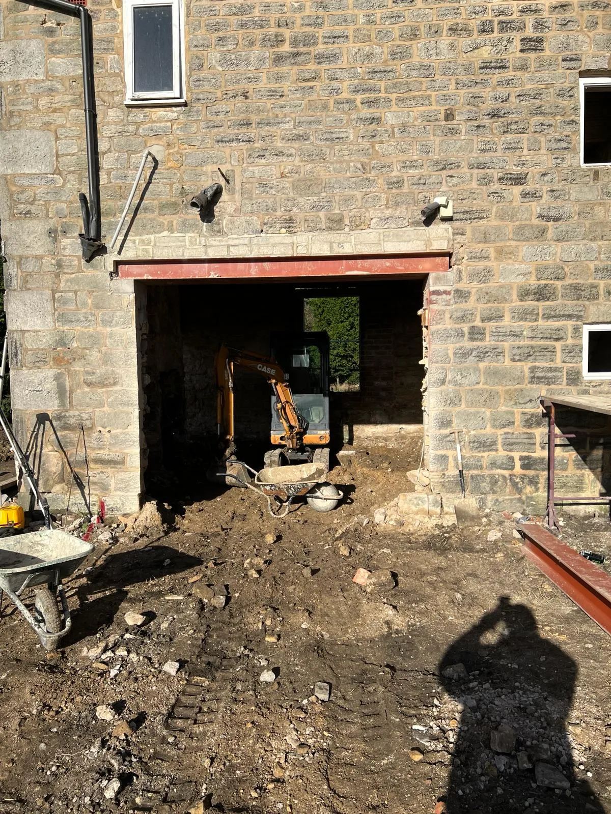 A construction site with a wheelbarrow in front of a brick building.