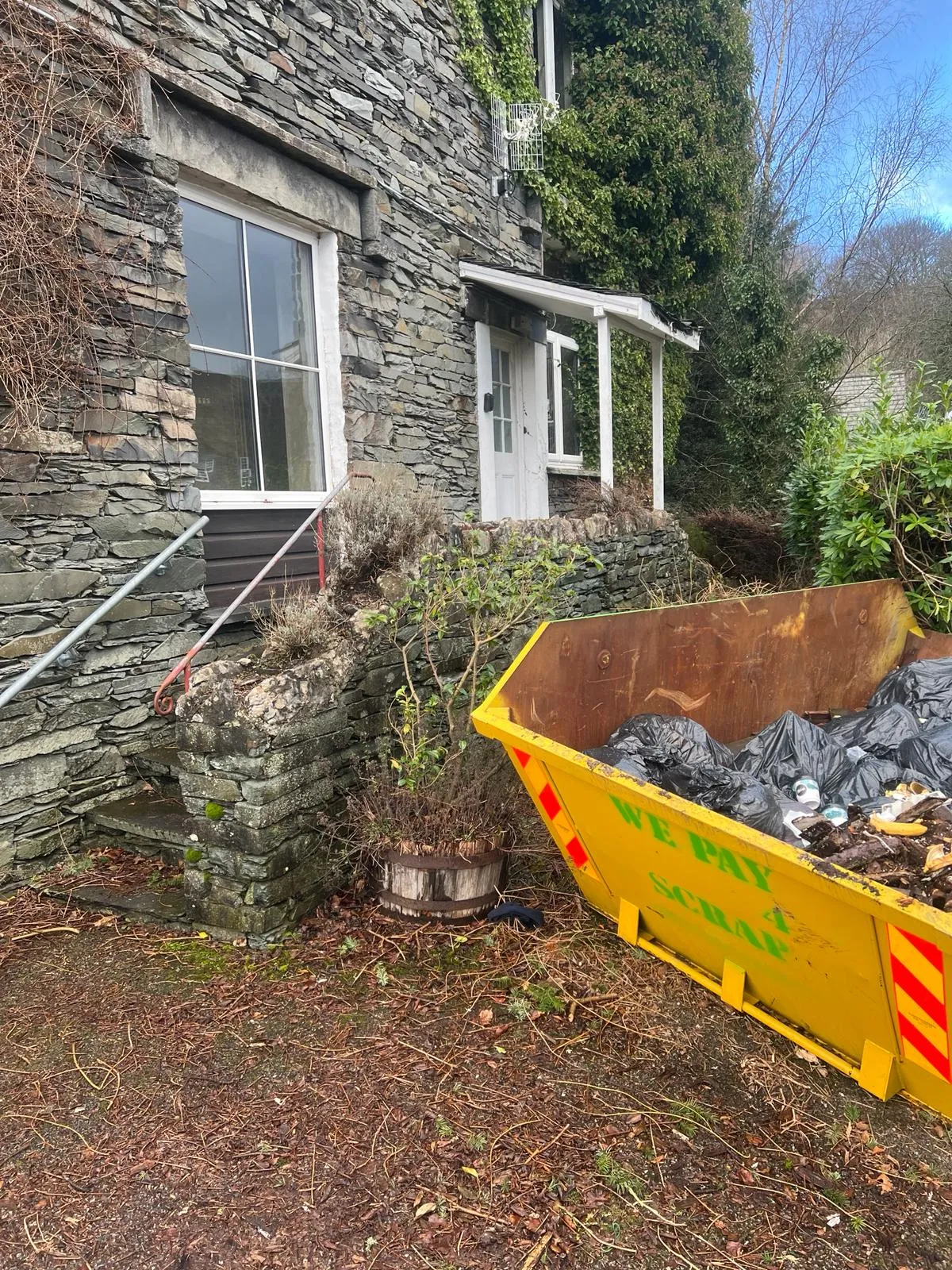 A yellow wheelbarrow filled with garbage in front of a house.